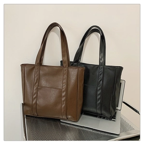 Detail view of brown and black pleated faux leather tote bags with front pockets