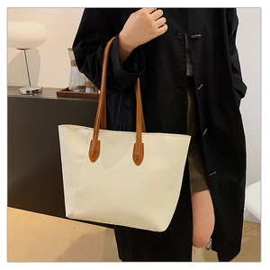Detail of minimalist cream tote bag with brown handles showing stitching and texture