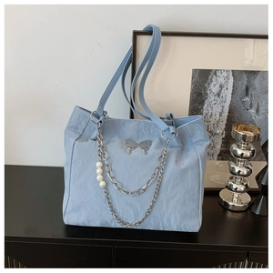 Close-up of light blue tote bag featuring a silver butterfly buckle and pearl chain detail