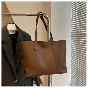 Detail der dunkelbraunen Leder-Shopper-Tasche mit vertikalen Nähten vor grauem Blazer
