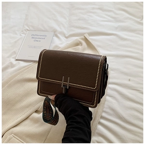 Detail of dark brown retro shoulder bag with gold metal rivets and woven strap