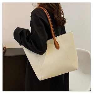 Detailed side view of a large cream tote bag with dark brown straps worn by a model
