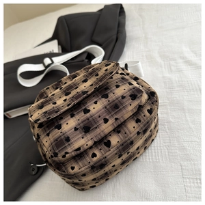 Detail of coffee plaid crossbody bag featuring black hearts and white fabric strap