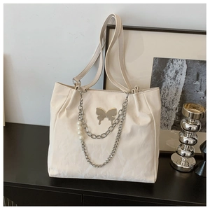Detail view of cream tote bag with silver butterfly charm and pearl metal chain