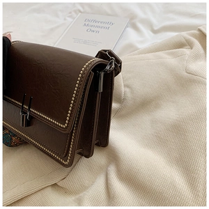 Close-up of vintage dark brown crossbody bag with gold rivets and multi-layer gussets