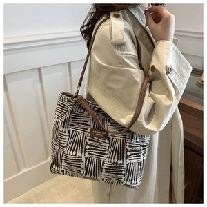 Detail view of woven geometric pattern and leather brand tag on a stylish tote bag