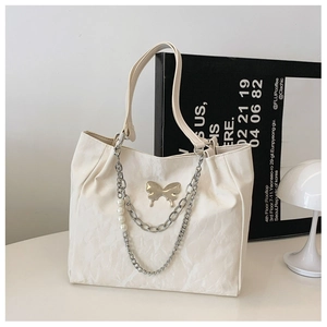 Close-up of beige tote bag with silver butterfly charm, metal chain and pearl detail