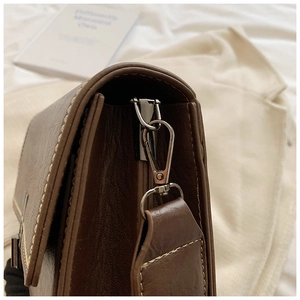 Detail of dark brown leather shoulder bag with contrast stitching and metal hardware