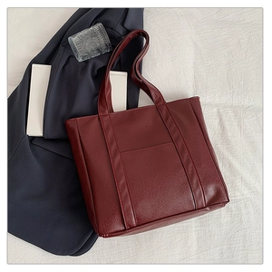 Deep burgundy tote bag with front pocket displayed on fabric with lifestyle props