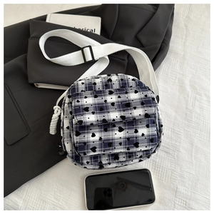 Detail of round plaid crossbody bag with black heart prints and white cotton strap