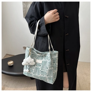 Detail of green and white striped woven tote bag with a plush cloud charm on shoulder strap