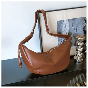 Detail of soft brown crescent bag with matte leather texture and metal buckle on black desk