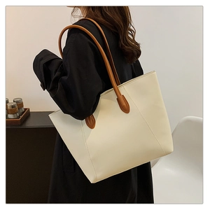 Minimalist beige leather tote bag with brown straps shown on shoulder for daily commute