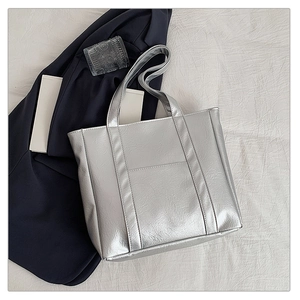Detail shot of a silver metallic tote bag with crinkled texture on a fabric background