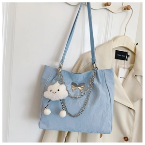 Detailed view of light blue tote bag with silver chain, metallic bow, and cloud charm