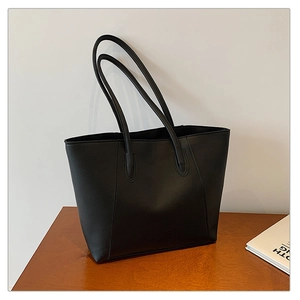 Minimalist black matte leather tote bag placed on a wooden desk in a modern interior setting