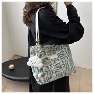 Detail of green and white woven tote bag featuring leather straps and cloud charm accessory