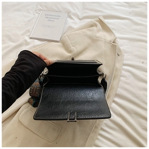 Detail of black embossed leather crossbody bag with dual compartments and silk scarf accent