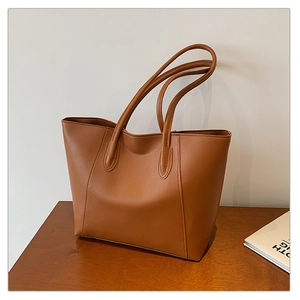 Detail of brown matte faux leather tote bag with vertical stitching on wooden desk