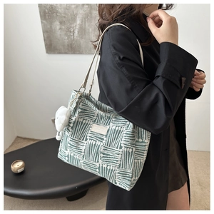 Detail of green and white woven tote bag with white leather strap and plush ball charm