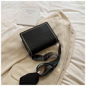 Detail of black rectangular crossbody bag with rivets and vintage ethnic style wide strap