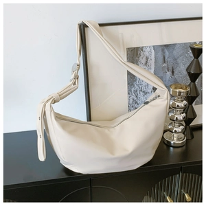 Detail of cream-colored crescent bag with knotted wide strap and metal buckle