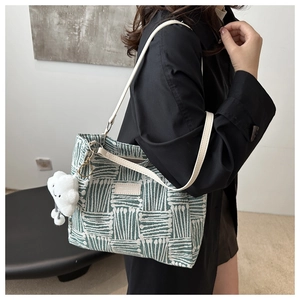 Detail of woven green and white tote bag with leather strap and cloud charm accessory