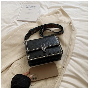 Detail of black pebbled leather crossbody bag with ethnic strap and metal studs