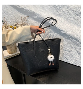 Detail of black tote bag with embossed texture and a white plush doll charm