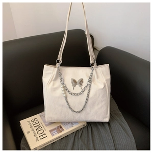 Detail of white tote bag featuring silver butterfly charm, metal chains and pearl pendant