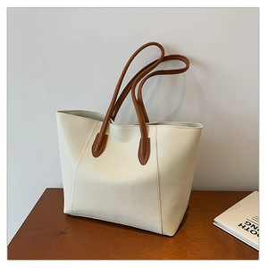 Detail of minimalist cream tote bag with dark brown straps and stitching on wooden surface