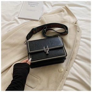 Detail of vintage black faux leather crossbody bag with metal rivets and jacquard strap