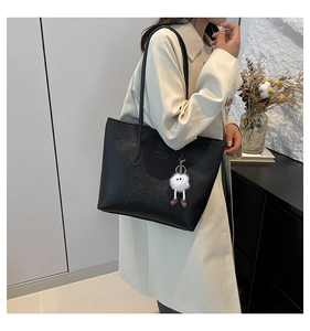 Detail of black leather tote bag with embossed cartoon pattern and plush charm pendant
