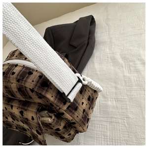 Detail of brown plaid crossbody bag with black heart prints and wide woven strap