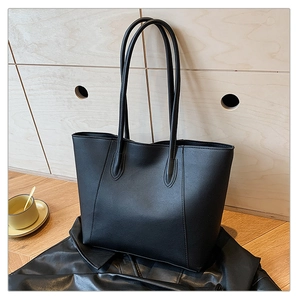 Detail of a black leather tote bag with vertical stitching and slim shoulder straps