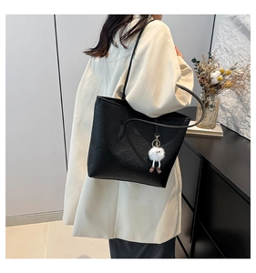 Detail of black embossed tote bag with cartoon patterns and white fur ball keychain