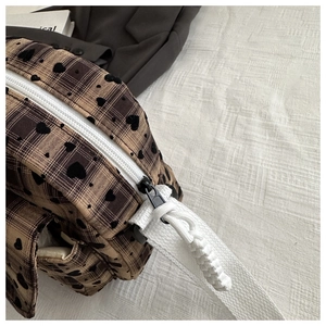 Detail of brown plaid bag featuring black hearts, white zipper and woven shoulder strap