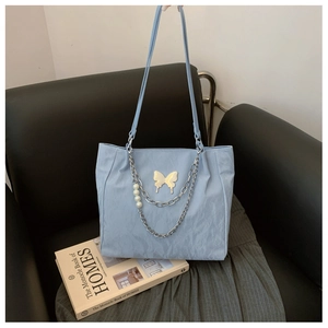 Detail of light blue tote bag with metallic butterfly and pearl chain on a leather sofa