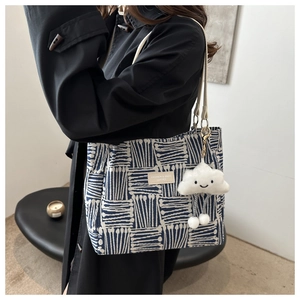 Detail of blue grid canvas tote bag with leather logo patch and white cloud charm