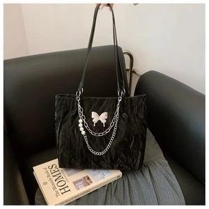 Detailed view of black pleated tote bag featuring silver butterfly and pearl chain charms