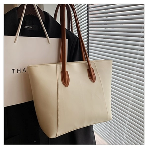 Detail of cream tote bag with vertical stitching and brown leather handles in natural light