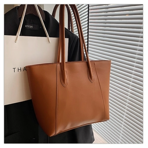 Detail of a brown leather tote bag showing fine stitching and matte texture in natural light