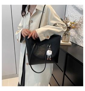 Close-up of black leather tote with embossed cartoon patterns and plush charm on the shoulder