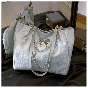 Detail of silver metallic tote bag featuring butterfly charm and pearl chain accent