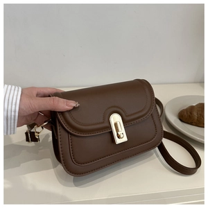 Detail showing hand holding a dark brown matte leather flap crossbody bag with gold buckle