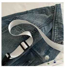 Detail of blue denim bag featuring durable white woven shoulder strap and plastic buckle
