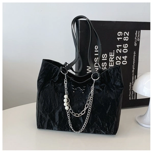 Close-up of black pleated tote bag featuring silver chain and pearl pendant detail