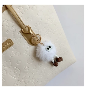 Close-up of embossed cream tote bag featuring cute plush monster charm and PU leather texture