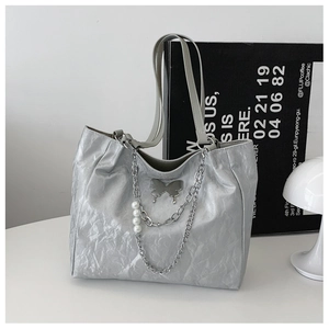 Close-up of silver pleated tote bag featuring metal butterfly and pearl chain charms