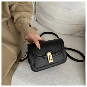 Detail of matte black leather bag with gold metal lock and curved flap design